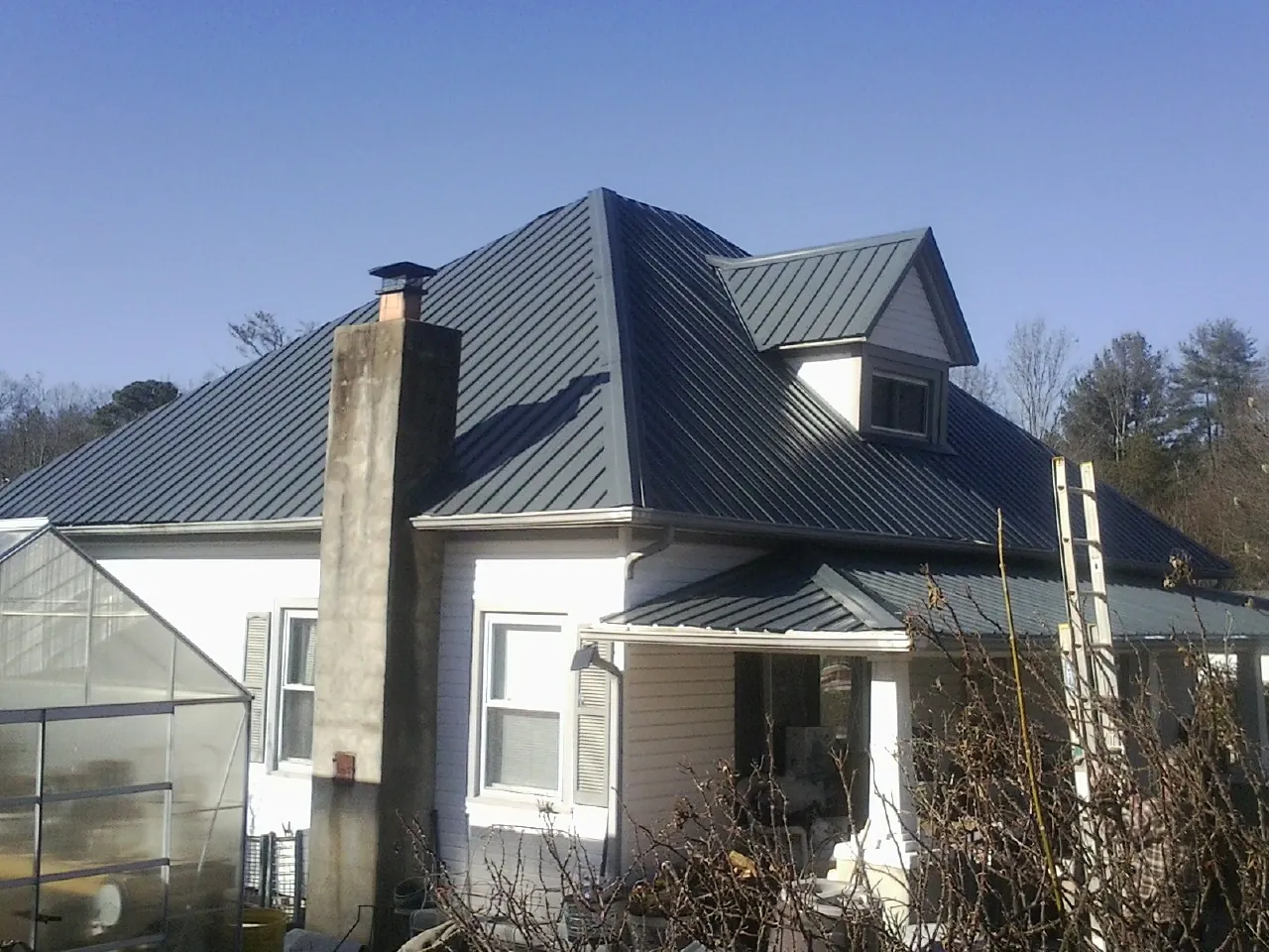 Dark blue standing seam metal roof on a white farmhouse with dormer — Slate & Tile Roof Repair by Roofing Brothers in Cana