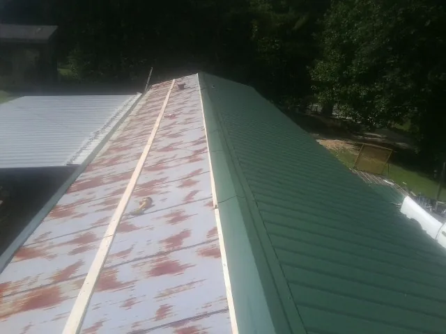 Old rusted panels beside newly installed green metal roofing — Wind Damage Roof Repair by Roofing Brothers in Cana