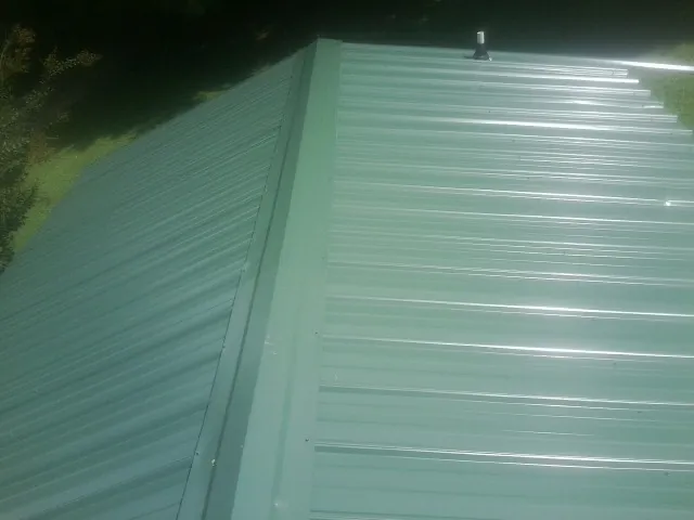 New green metal panels meeting at the ridge of a roof — Flat Roof Repair work by our crew in Cana