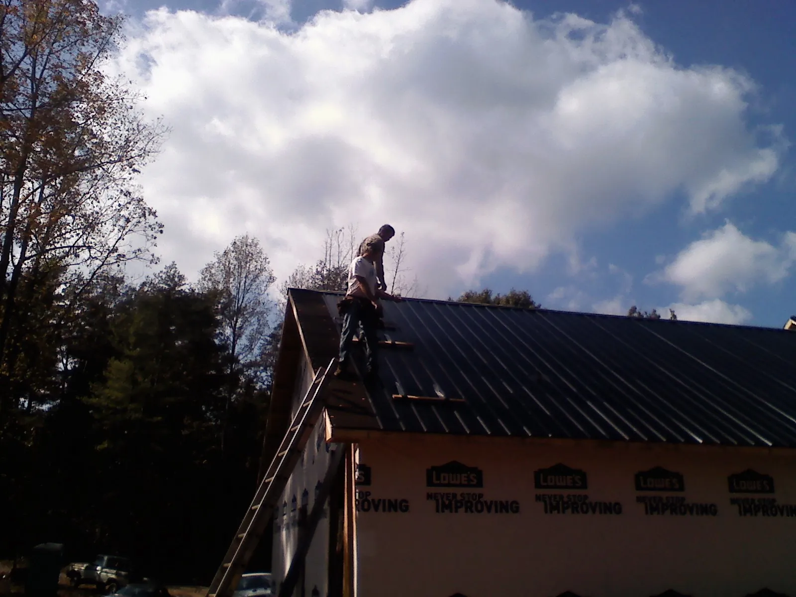 Roofer fastening dark metal panels high against a cloudy sky, from a Roof Inspection job in Cana