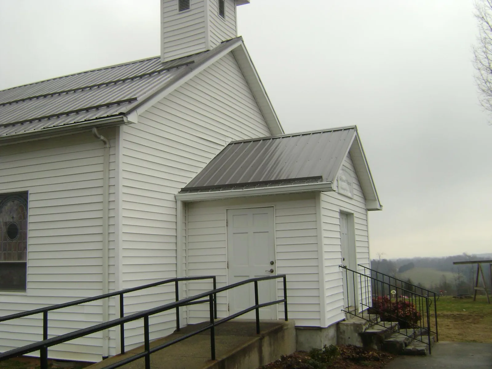 Gray metal roof on a white clapboard church with a steeple in Cana