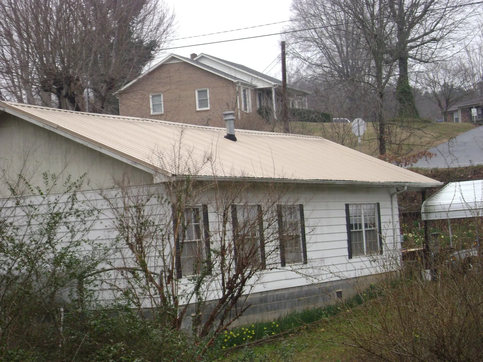 Tan metal roof on a white sided house set into a hillside — Commercial Roofing by Roofing Brothers in Cana