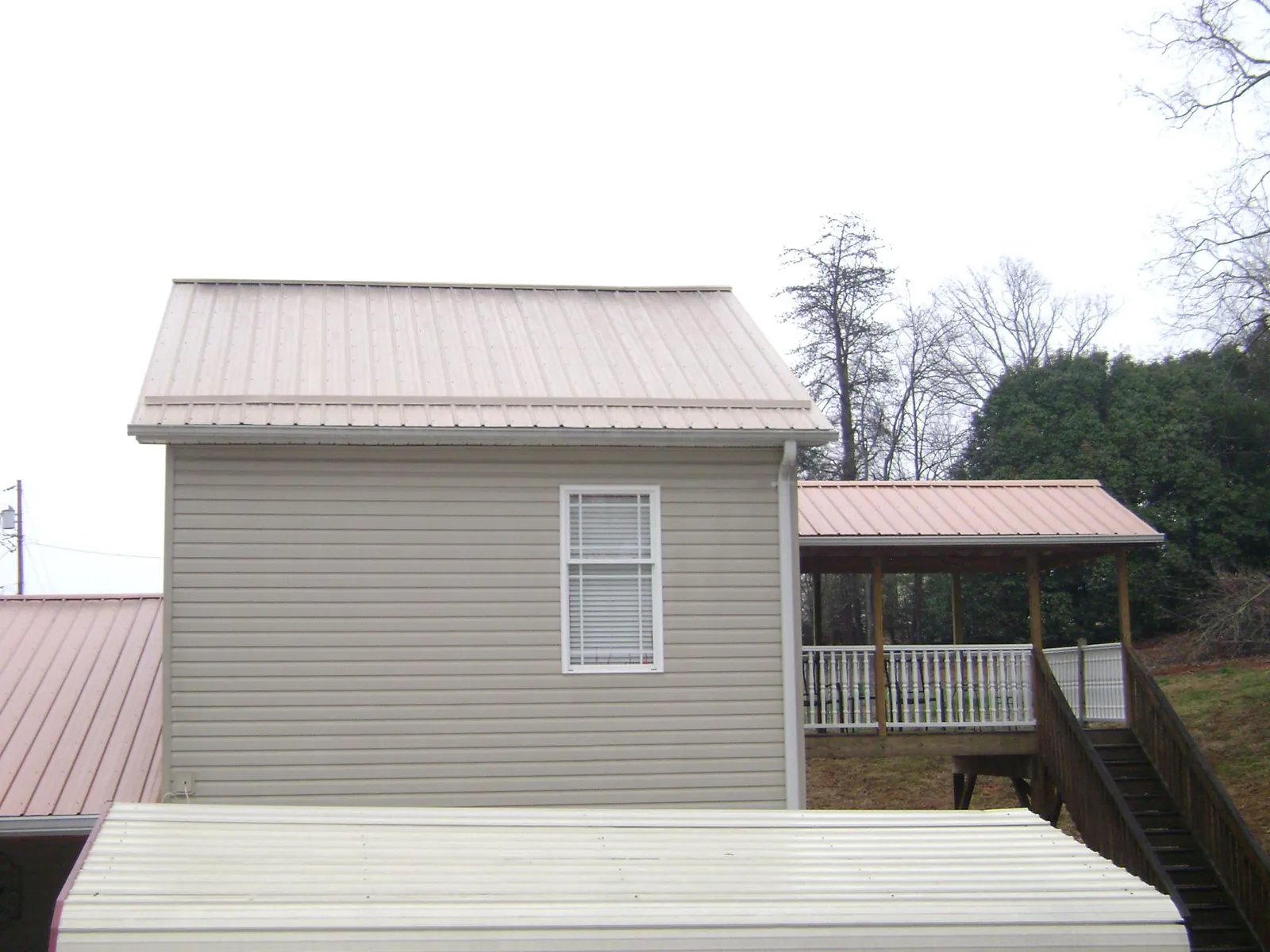 Tan metal roofs on a two story addition and attached porch, from a Roof Replacement job in Cana